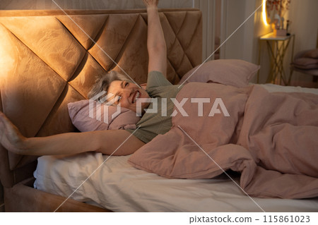 An elderly woman wakes up in bed after a long night's sleep. She's still in her pajamas and hugging a pillow with her arms. The camera focuses on her face as she slowly opens her eyes. An elderly woman wakes up in bed after a long night's sleep. She's still in her pajamas and hugging a pillow with her arms. The camera focuses on her face as she slowly opens her eyes. 115861023