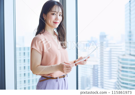 A woman looking at documents by the window in an office 115861973