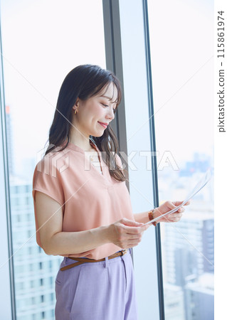 A woman looking at documents by the window in an office 115861974