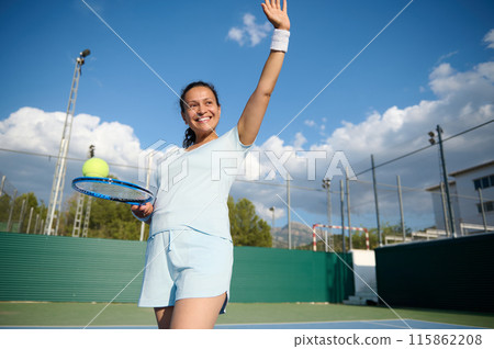 Healthy middle-aged woman playing tennis on an outdoor court and smiling 115862208