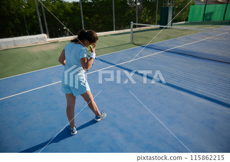 Woman in her 40s playing tennis on a sunny outdoor court 115862215