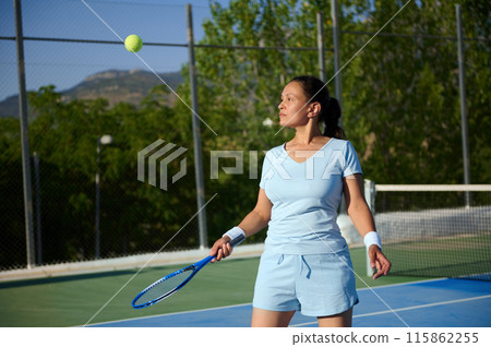 Woman in her 40s playing tennis on a court, focusing on the ball Woman in her 40s playing tennis on a court, focusing on the ball 115862255