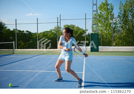 Middle-aged woman playing tennis on an outdoor court on a sunny day 115862270