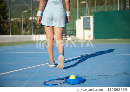 Middle-aged woman tennis player walking on outdoor tennis court Middle-aged woman tennis player walking on outdoor tennis court 115862289