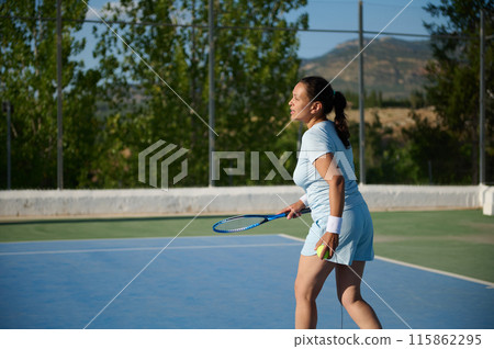 Middle-aged woman playing tennis on an outdoor court on a sunny day 115862295