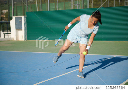 Middle-aged woman playing tennis on outdoor court, practicing forehand swing 115862364