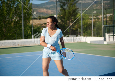 Middle-aged woman playing tennis on outdoor court during a sunny day 115862366