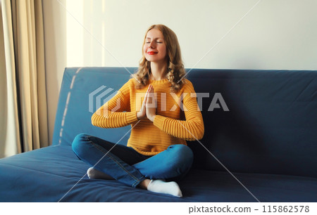 Calm relaxed healthy young woman meditates, girl practicing doing yoga sitting on the couch at home Calm relaxed healthy young woman meditates, girl practicing doing yoga sitting on the couch at home 115862578