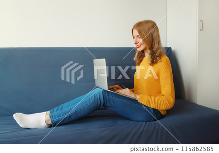 Happy modern young woman working on a laptop, freelancer girl sitting on a couch in the living room 115862585