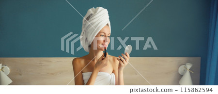 Beautiful young woman painting her lips with red lipstick applying makeup looking in pocket mirror 115862594