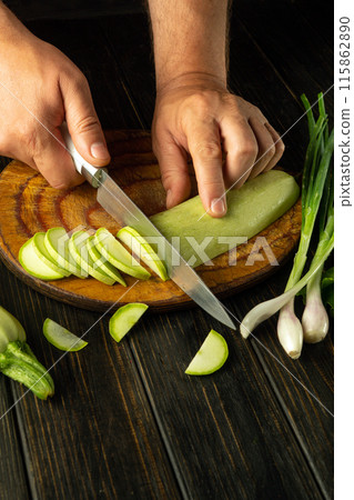 The cook cuts the zucchini. Cooking marrow with vegetables and spices on the kitchen table for a diet lunch. Advertising space 115862890