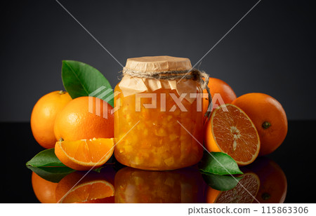 Orange jam in glass jar and fresh fruits on a black reflective background. 115863306