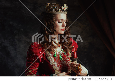 pensive medieval queen in red dress with candle and crown 115863704