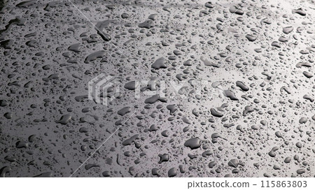 This image captures raindrops on a dark surface, highlighting their glistening clarity and natural beauty. 115863803