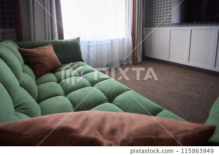 A stylishly decorated modern living room features a green sofa with cozy brown pillows 115863949