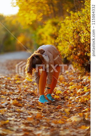 elegant woman in fitness clothes in park tying shoelaces 115864332