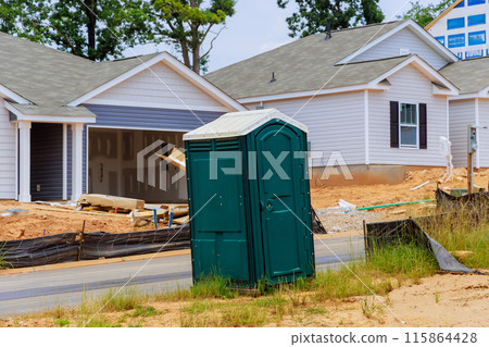 During construction of house, portable plastic bio toilet cabins stalls are located on construction site 115864428