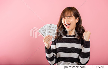 Asian happy portrait beautiful young woman standing smile her celebrating holding dollar money fan banknotes on hand and looking to camera on pink background with copy space for text 115865709