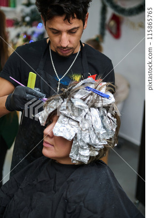 Hairdresser applying dye to woman's hair with foil highlights 115865765