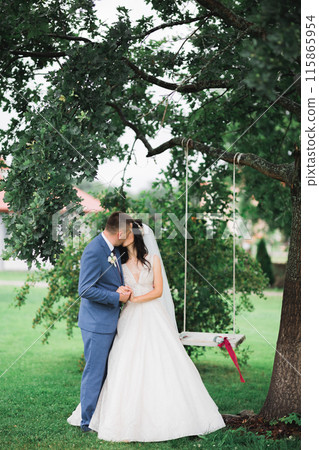 Romantic, fairytale, happy newlywed couple hugging and kissing in a park, trees in background 115865954
