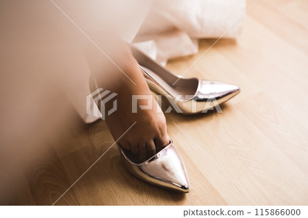 Bride puts on elegant and stylish bridal shoes on her tender feet 115866000