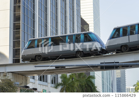 Public transportation in downtown Miami in Florida USA. Metrorail city train car on high railroad over street traffic between skyscraper buildings in modern American megapolis 115866429
