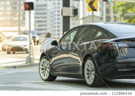 Electric car on Miami street. Traffic with driving cars at urban intersection with traffic lights in Florida Electric car on Miami street. Traffic with driving cars at urban intersection with traffic lights in Florida 115866439