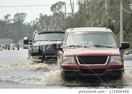 Hurricane flooded street with moving cars and surrounded with water houses in Florida residential area. Consequences of natural disaster 115866480