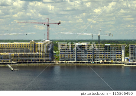 Tower lifting cranes at high residential apartment buildings construction site. Real estate development on sea shore 115866490