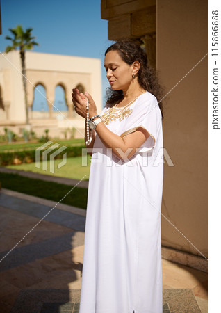 Woman in white traditional dress praying outdoors with rosary beads Woman in white traditional dress praying outdoors with rosary beads 115866888