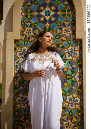Woman in traditional white dress standing by colorful mosaic wall on a sunny day Woman in traditional white dress standing by colorful mosaic wall on a sunny day 115866902
