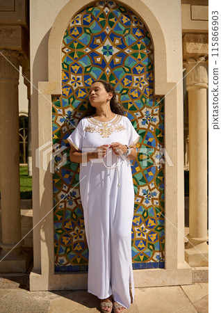 Woman in white dress standing by a colorful mosaic wall at a mosque Woman in white dress standing by a colorful mosaic wall at a mosque 115866903