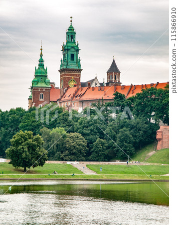 Wawel Castle stands majestically above the Vistula River banks on a sunny summer day, with greenery surrounding the historic Polish landmark. Krakow, Poland Wawel Castle stands majestically above the Vistula River banks on a sunny summer day, with greenery surrounding the historic Polish landmark. Krakow, Poland 115866910