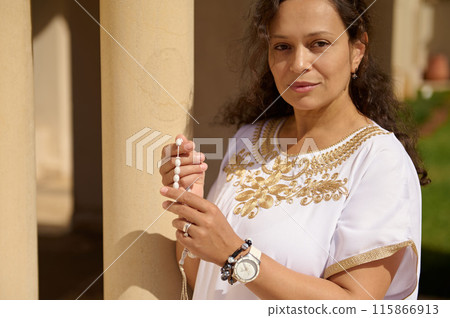 Woman holding prayer beads in a serene outdoor setting, spiritual and contemplative moment 115866913