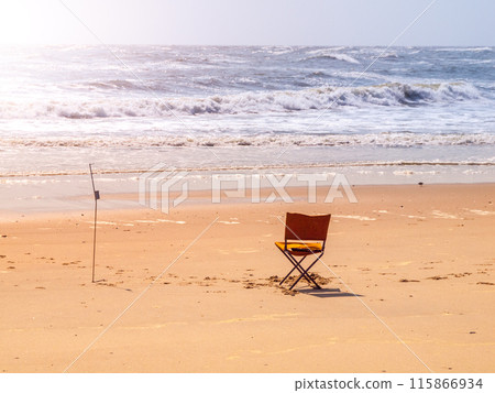 A single chair faces the turbulent waves of a beach in Namibia, capturing the solitude and beauty of the seaside at dusk. 115866934