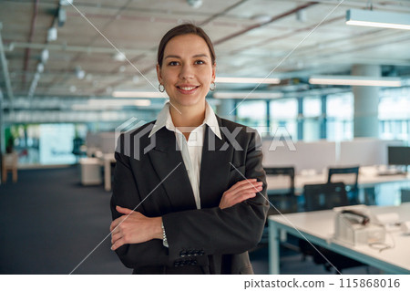A confident businesswoman is standing and posing in a modern office environment 115868016