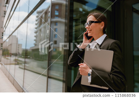 A confident businesswoman is multitasking, talking on the phone and holding a laptop 115868036
