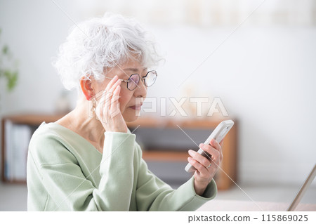 Smiling senior woman holding a smartphone (smartphone) Profile of a woman struggling to see the smartphone due to presbyopia 115869025