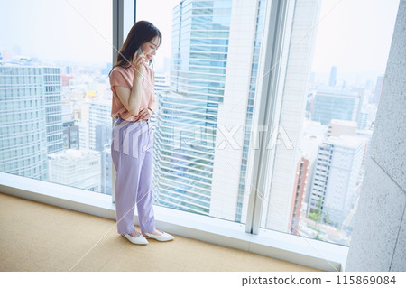 Woman making a phone call by the window in the office Woman making a phone call by the window in the office 115869084