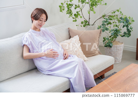 A pregnant woman touching her belly with a smile A pregnant woman touching her belly with a smile 115869777