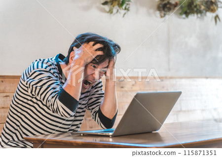 Asian man holding his head while looking at a computer in a cafe or restaurant (stocks, investment, crash, loss) Asian man holding his head while looking at a computer in a cafe or restaurant (stocks, investment, crash, loss) 115871351
