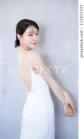 The upper body of a woman wearing a beautiful white dress with an open back, looking at the camera. Image of beauty treatment, hair removal, and slimming. The upper body of a woman wearing a beautiful white dress with an open back, looking at the camera. Image of beauty treatment, hair removal, and slimming. 115872335