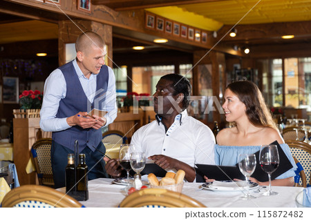 Male waiter carrying order for visitors in restaurant Male waiter carrying order for visitors in restaurant 115872482