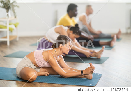 Young woman coach and students perform Janu Shirshasana during training in studio 115872554