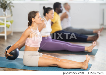 Young woman doing exercises with ball during group Pilates session Young woman doing exercises with ball during group Pilates session 115872578