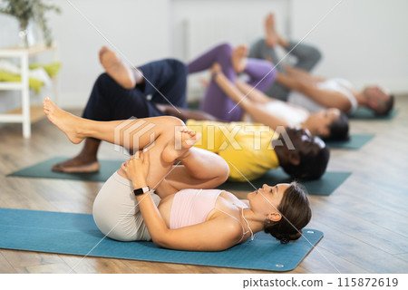 Young woman coach and students perform Supta kapotasana during training in studio Young woman coach and students perform Supta kapotasana during training in studio 115872619
