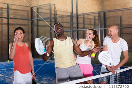 Four smiling men and women with padel rackets posing at court Four smiling men and women with padel rackets posing at court 115872700