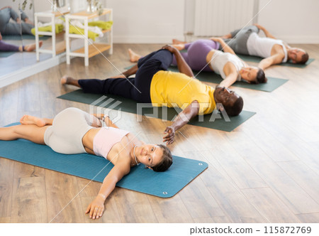 Girl performing Supta Matsyendrasana during group yoga session Girl performing Supta Matsyendrasana during group yoga session 115872769