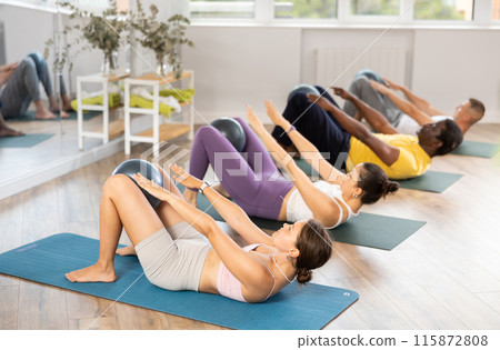Men and girls hold fitball in their lap, raise and lower torso 115872808
