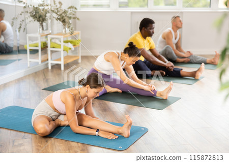 Young woman doing Janu Sirsasana in group yoga class Young woman doing Janu Sirsasana in group yoga class 115872813